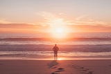 A calm person stands on the beach looking out to sea