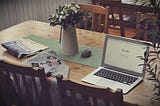 wood dining room table with open laptop and newspaper on it.