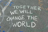 A photo of a sidewalk, with the words “together we will change the world” written in chalk