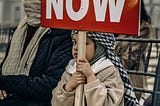 Palestinian child holding a sign saying ceasefire now.
