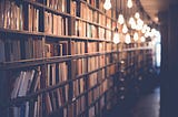 Shelves filled with books in a library, lit by low hanging lightbulbs