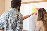 a group of 3 young professionals looking at a white board with sticky notes