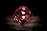 A red die being rolled and showing three dots in front of a black background