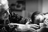 An elderly woman reaches out to a sleepy baby.