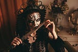 A woman dressed in black with eyes outlined in black holds a knife to her lips