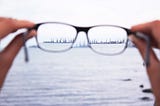 A pair of glasses in the foreground focus to reveal machinery in the ocean in the background