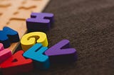 Colourful toy letters scrambled over a wooden board and a fabric patch. H, G, V, F, A, N (partially)