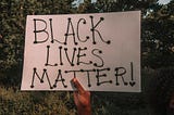 A hand holding a poster which says “Black Lives Matter”