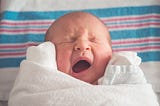 Colour photo of a swaddled newborn baby yawning.