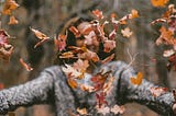 a woman with arms exttended delights in falling leaves