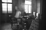 A noir-ish office in which a desk, typewriter and some bottles are visible. It could belong to a weary reporter or a cynical private eye, who knows?