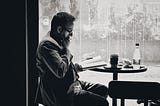 A man sitting on his desk reading and meditating with a cup of coffee and a bottle of water.