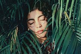 A woman laying in quiet contemplation behind palm fronds and leaves