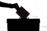 Black and white image of someone placing a paper ballot into a ballot box.