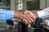 Two people of color in long sleeve shirts shaking hands