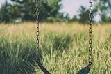 An empty swing in front of tall grass