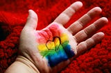 A hand with the rainbow flag painted. A heart is drawn in the centre