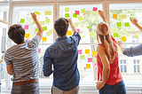 Equipe trabalhando com post-its em um painel de vidro.