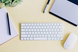 desk with keyboard, mouse, pens, notebook, and small plant