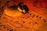 A glowing gold ring with Elvish inscriptions rests on a rock, placed over a map of Mordor from “The Lord of the Rings,” illuminated by fiery orange and red light.