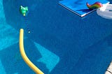 An empty pool with a yellow foam noodle and various other pool toys