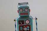 A close up photo of a blue robot toy. It has dials and clock work stickers on its metal riveted torso. The expression on its face could be interpreted to be creepy.