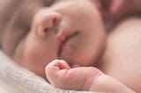 Baby, asleep. Face and chest in the background, hand in the foreground.