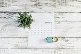January calendar on a wooden background with plant and clock.