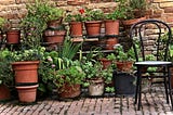 A series of several layers of terracotta pots forming a  garden, with paving and a chair.