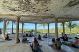 A yoga class as the abandoned Sailing club, with a view of the bay and sailboats.