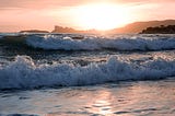 Waves crashing on sea shore. Sun rising in background.