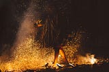 A person in shadows walking across fire-lit coals