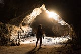 A Lady standing in a cave look at the light that peeps in