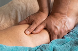 An image of a person massaging another individual’s leg.