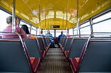 Inside a bus with seats on each side and a few seated passengers.