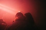 a man and a woman kiss in the red lighting of a club