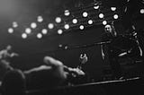 Black and white photo of a wrestler grabbing his throat on the ring floor, the ref nearby and counting him out.