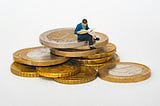 Small man sitting on gold coins…