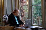 man writing on a laptop. he’s sitting near a window. we can’t see his screen but we can only guess he’s reading smillew’s substack smillew.substack.com/