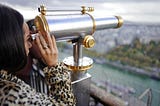 A Black woman looking through a telescope.