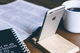 Picture showing a phone in the foreground on the table. In the background, there is a book.