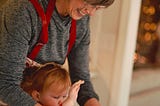 A grandma with a little girl, both wearing aprons, shaping together a ball of dough.