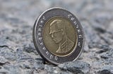 A coin with a head on it sits on a stone surface. The head is a man wearing glasses