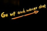 Go up and never stop written in form of a neon sign with an arrow pointing upward.