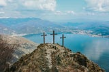 three crosses on the top of a mountain with a blue sky and clouds background