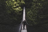 A man hiking across a bridge in the forest.