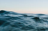 A picture of the ocean from the perspective of someone in the water, with a light gray-to-pink sky above.