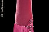 A photograph of an antique pink flapper dress, now preserved in a museum. The date of the dress’s creation is listed as 1925.