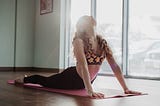 Lady doing a yoga pose with the sun shining in through the window.