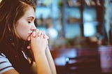 Woman holding her hands together with eyes closed. Looks like she is meditating or praying.